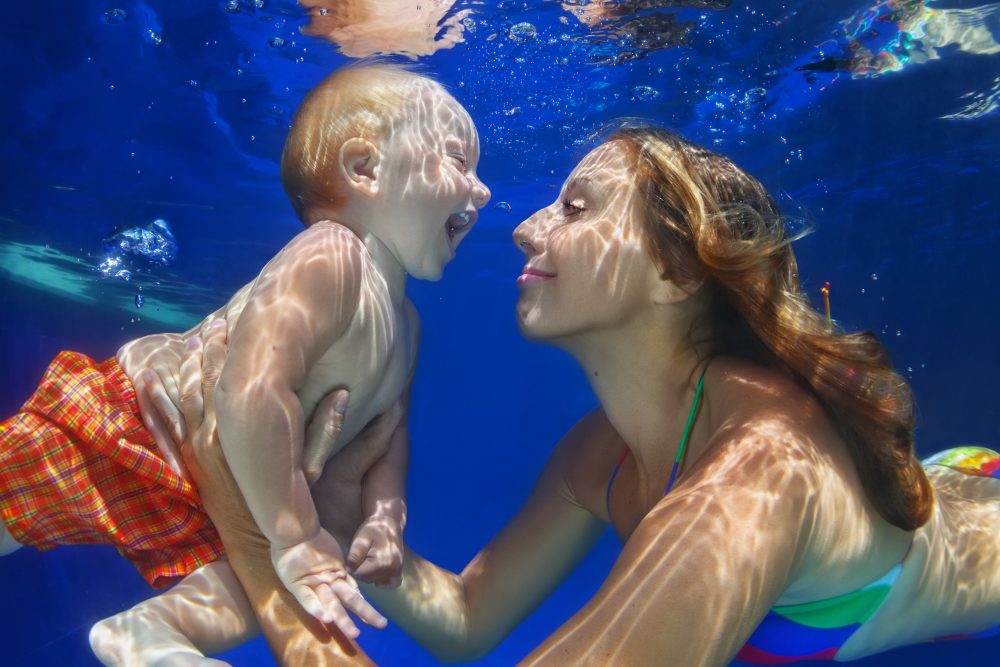 Mother, baby son swim and dive underwater in swimming pool